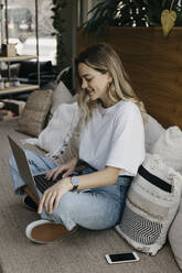 Lächelnde junge Frau, die einen Laptop benutzt und auf dem Sofa sitzt - LHPF01318