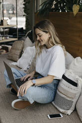 Smiling young woman using laptop while sitting on sofa - LHPF01318