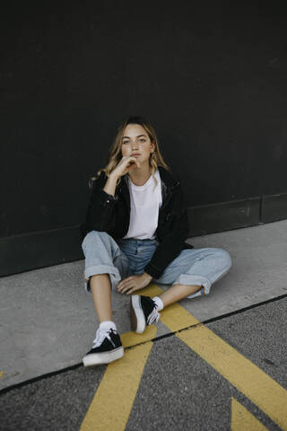 Thoughtful woman with hand on chin sitting against wall stock photo