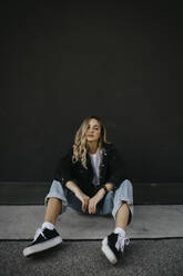 Woman sitting on footpath against wall - LHPF01329