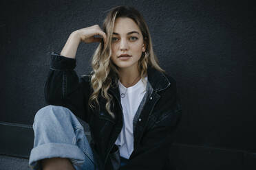 Beautiful woman with hand in hair sitting against wall - LHPF01330