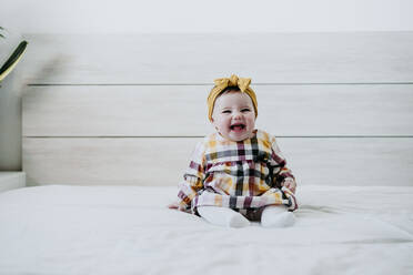 Cheerful baby girl sitting on bed at home - EBBF01057