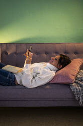 Frau benutzt Smartphone, während sie zu Hause auf dem Sofa liegt - GIOF09300
