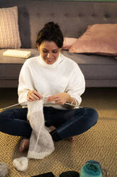 Smiling mid adult woman knitting wool at home - GIOF09302