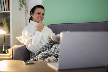 Mid adult woman eating food while using laptop sitting at home - GIOF09309