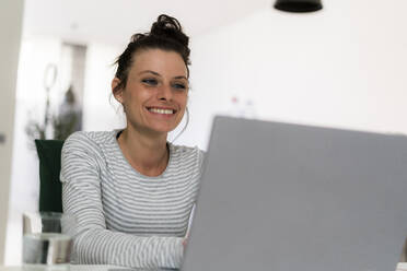 Lächelnde Frau, die zu Hause sitzend am Laptop arbeitet - GIOF09317