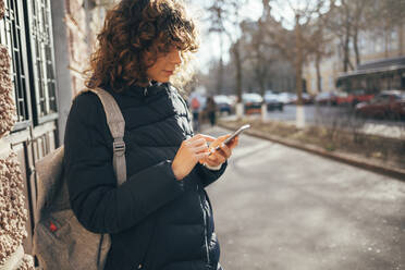 Mittlere erwachsene Frau mit Tasche, die ein Mobiltelefon benutzt, während sie auf dem Bürgersteig in der Stadt steht - OYF00227