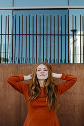 Beautiful fashionable woman standing with hands in hair against surrounding wall - TCEF01252