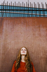 Redheaded beautiful woman leaning against a wall outdoors - TCEF01254