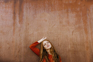 Young woman with eyes closed leaning on brown wall - TCEF01255