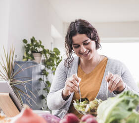 Smiling woman eating salad while sitting at home - UUF21939