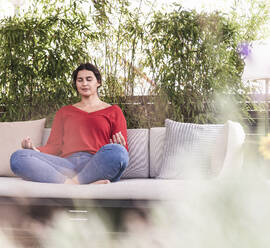 Young woman with eyes closed practicing yoga while sitting at backyard - UUF21944