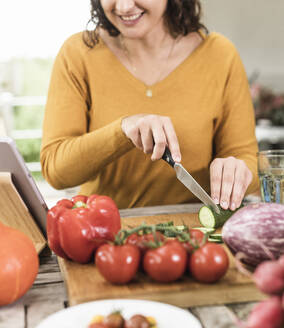 Lächelnde Frau schneidet Gemüse, während sie zu Hause am Tisch steht - UUF21946