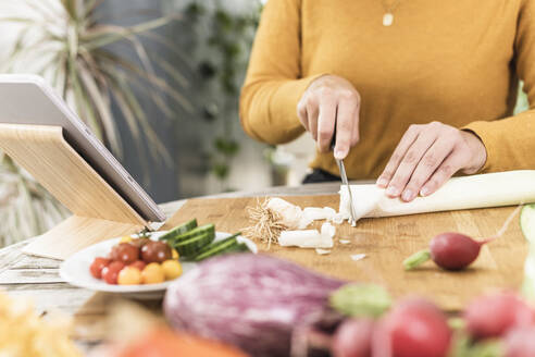 Woman cutting vegetable while standing by digital tablet on table at home - UUF21949