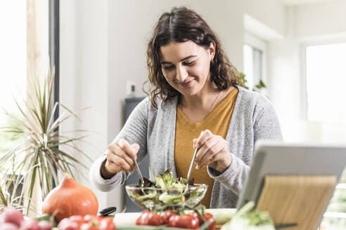 Smiling woman making salad while standing by table at home - UUF21950