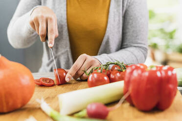 Junge Frau, die zu Hause am Tisch sitzend eine Tomate schneidet - UUF21954