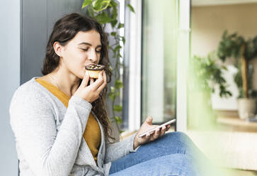 Young woman eating cupcake while sitting at home - UUF21959