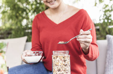 Smiling woman holding milk bowl preparing oats while sitting at backyard - UUF21969