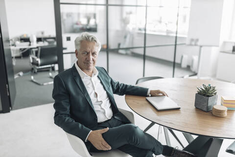 Selbstbewusster Geschäftsmann sitzt auf einem Stuhl am Tisch im Büro, lizenzfreies Stockfoto