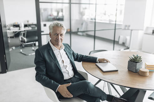 Confident businessman sitting on chair by table at office - GUSF04474