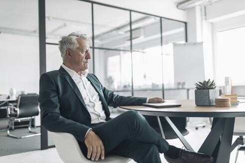 Businessman looking away while sitting on chair at office - GUSF04475