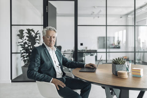 Senior man wearing suit using laptop while sitting on chair at office stock photo