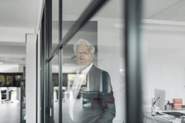 Geschäftsmann schaut weg, während er an einer Glaswand im Büro steht - GUSF04478