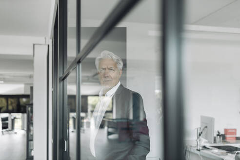 Businessman looking away while standing by glass wall at office - GUSF04478