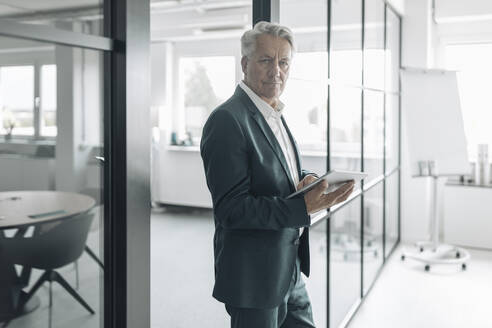 Geschäftsmann, der ein digitales Tablet benutzt, während er im Büro steht - GUSF04482
