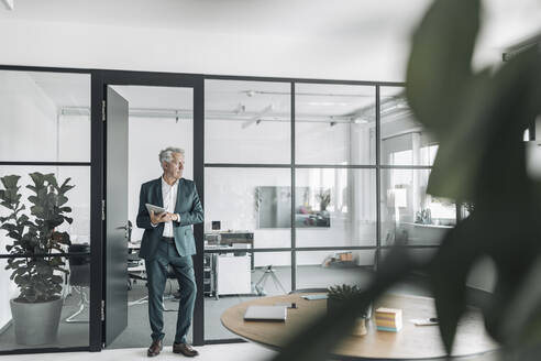 Businessman looking away while using digital tablet at office - GUSF04483