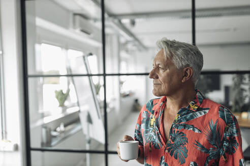 Businessman holding coffee cup while standing at office - GUSF04492