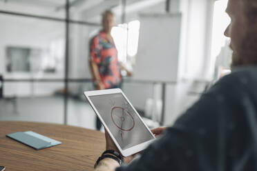 Colleague looking at diagram on digital tablet screen while sitting with businessman in background at office - GUSF04494