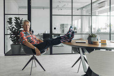 Businessman sitting with legs crossed on table at office - GUSF04499