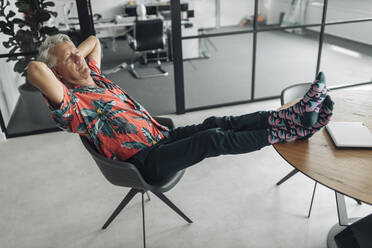 Businessman with hands behind hand resting on chair at office - GUSF04501