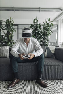 Businessman using virtual reality while playing video game at office - GUSF04505