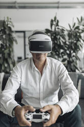 Businessman playing video game using virtual reality while sitting at office - GUSF04506