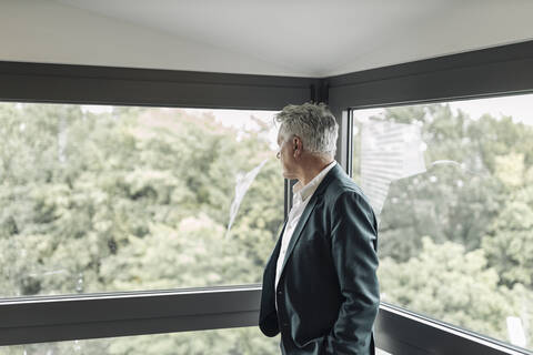 Businessman looking though window while standing at office stock photo