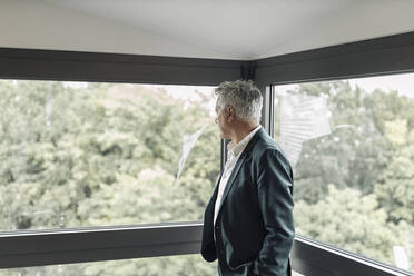 Businessman looking though window while standing at office - GUSF04514