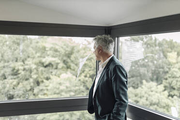 Geschäftsmann schaut durch das Fenster, während er im Büro steht - GUSF04514