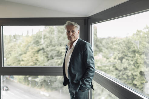 Businessman with hand in pockets standing by window at office - GUSF04515