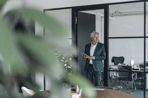 Businessman looking away while using digital tablet at office - GUSF04518