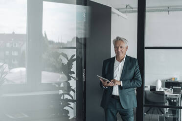 Smiling businessman using digital tablet while standing at office - GUSF04519