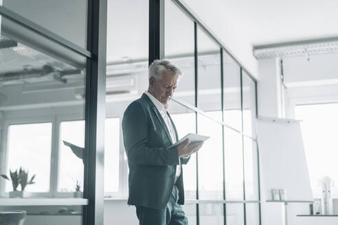 Businessman using digital tablet while standing by glass wall at office - GUSF04521