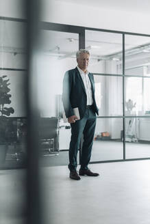 Man wearing suit holding digital tablet while standing at office - GUSF04526