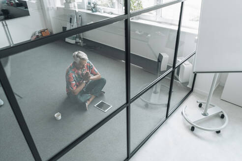 Businessman practicing yoga while sitting on floor at office - GUSF04539