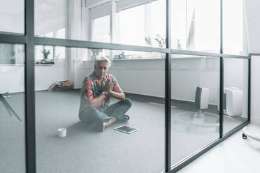 Businessman sitting in prayer position on floor at office - GUSF04540