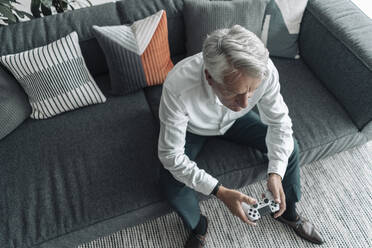 Geschäftsmann spielt ein Videospiel, während er auf dem Sofa im Büro sitzt - GUSF04542