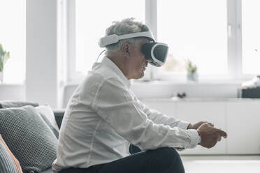 Businessman playing video game with virtual reality eyeglasses while sitting on sofa at office - GUSF04547