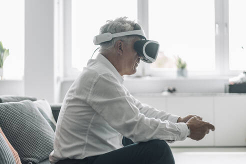 Geschäftsmann, der mit einer Virtual-Reality-Brille ein Videospiel spielt, während er auf dem Sofa im Büro sitzt - GUSF04547