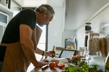 reifer Mann benutzt digitales Tablet, während er zu Hause in der Küche steht - VABF03662